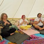 Three ladies sitting with hand to their hearts in ceremony space at the Conscious Heart Warriors healing village for festivals.