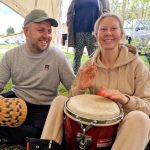 Man and lady smiling at a fox drum circle at the Conscious Heart Warrior's Healing village for festivals.