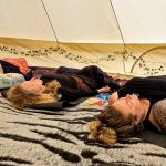 Three ladies laying down in Muladhara ceremony space at the Conscious Heart traveling healing village for festivals.