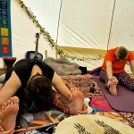 Two ladies in yoga pose in the Muladhara ceremony space at the Conscious Heart traveling healing village for festivals.