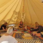 Group of people sitting in a circle at neckless making workshop at the Conscious Heart Warrior's healing village for festivals.