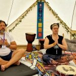 A man and lady sitting in a ceremony space with eyes closed holding their hands up to their heart at the Conscious Heart Warrior's healing village for festivals.